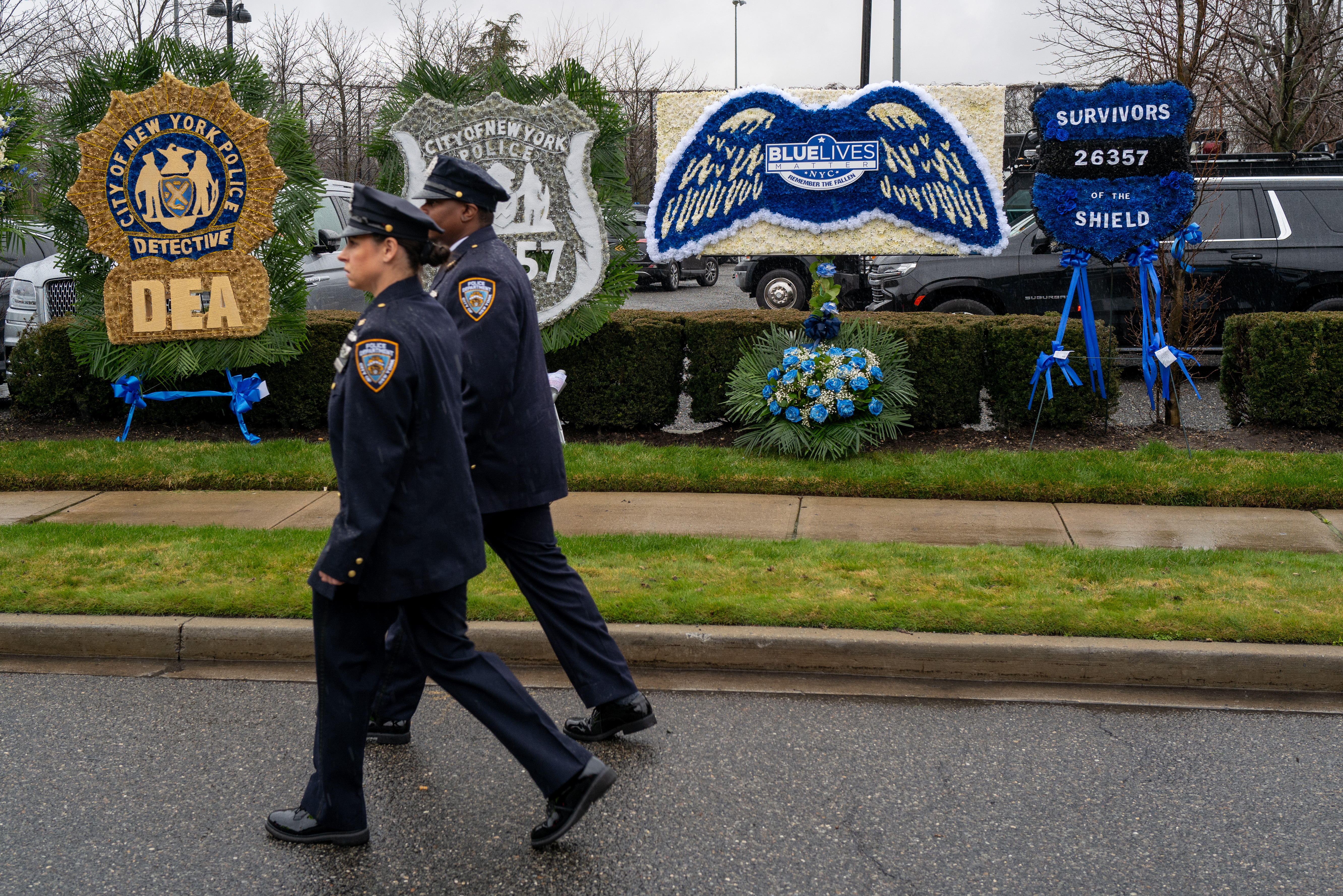 Two uniformed police officers walk past flowers and memorials for a fallen officer.