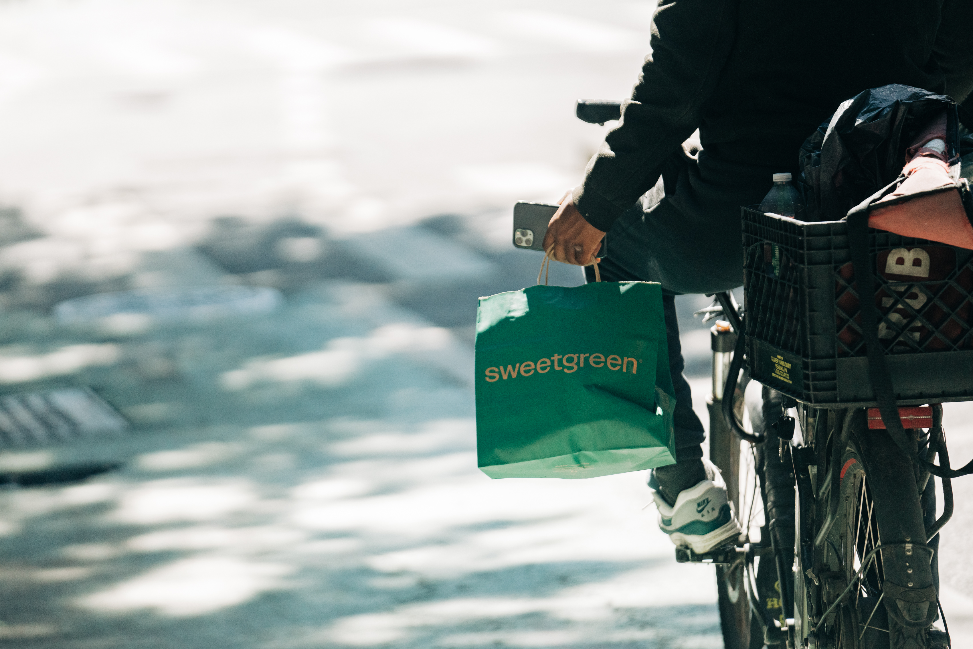 A person rides his bike holding a green delivery bag.