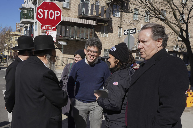 Council member Lincoln Rester, in a sweater and gray slacks, speaks to a handful of people on a city street.