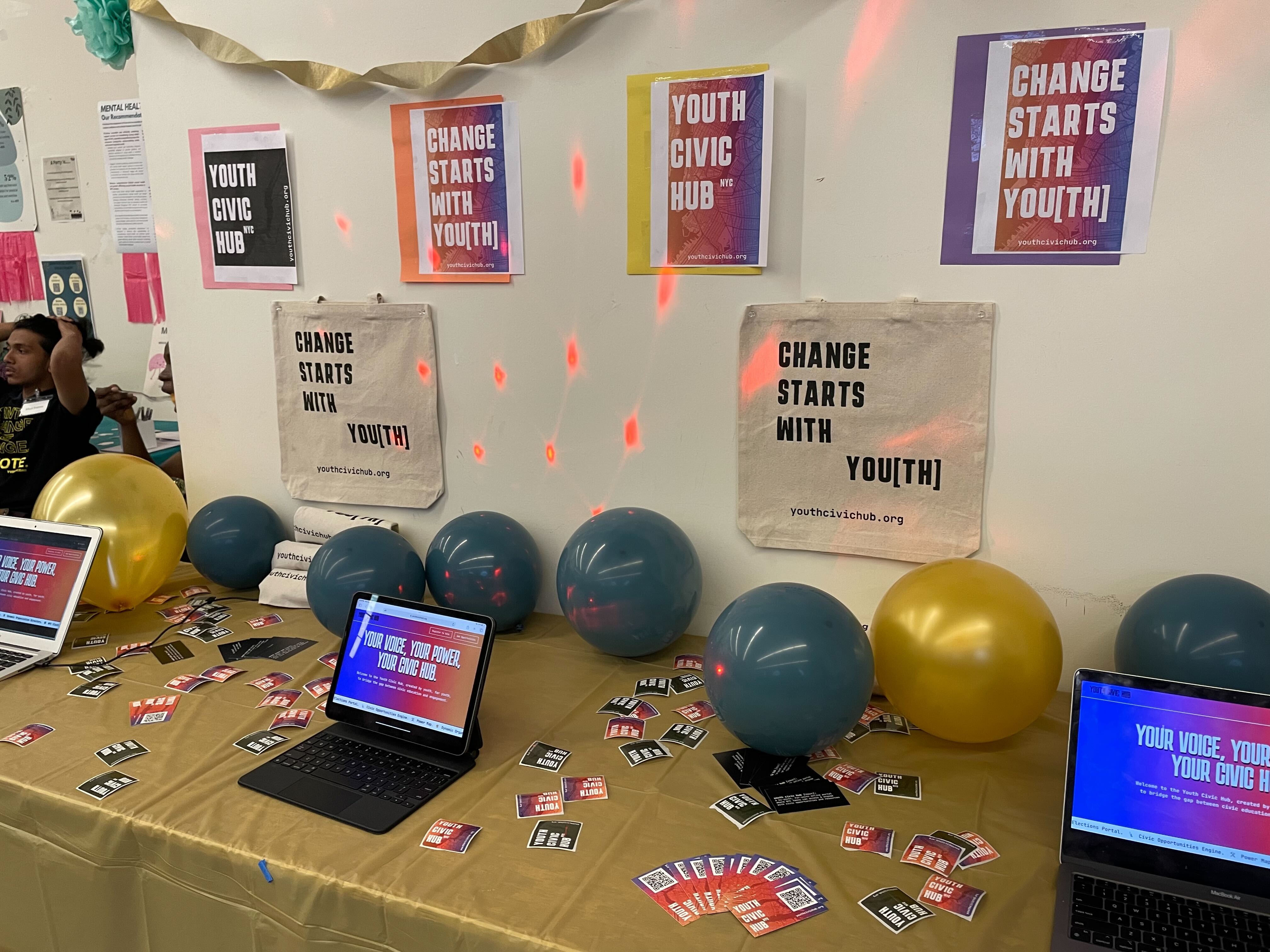 Balloons adorn a table that has laptops showing the civic engagement hub site.