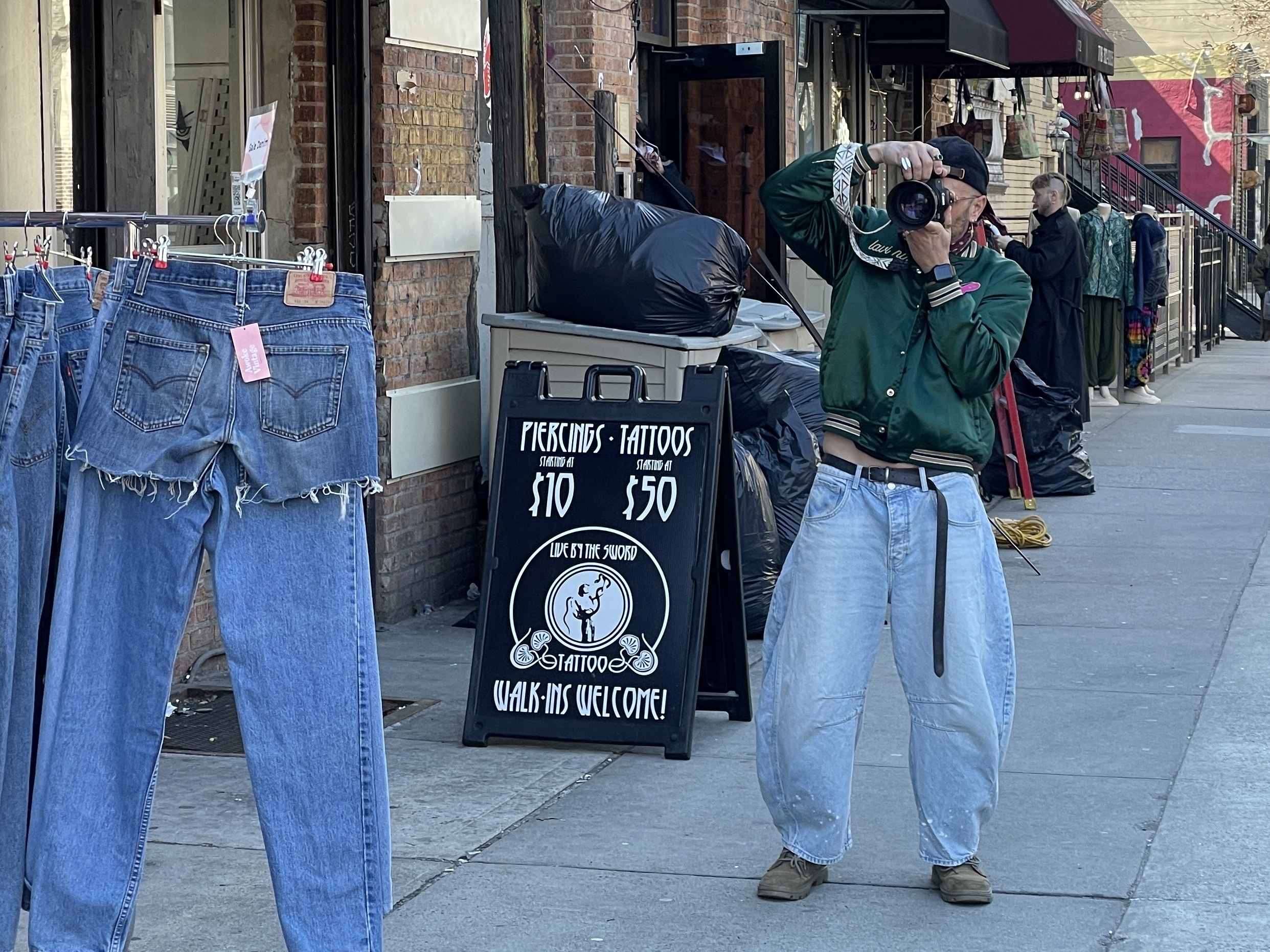 A man in a green jacket and jeans takes a picture.