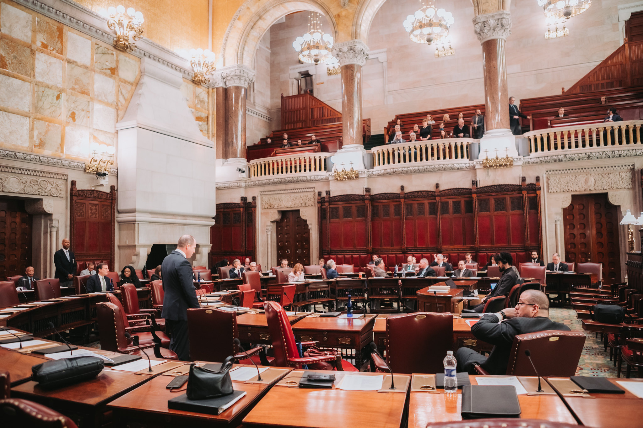 The New York state Senate chamber, an ornate space with marble walls and wooden desks, with a balcony for spectators.