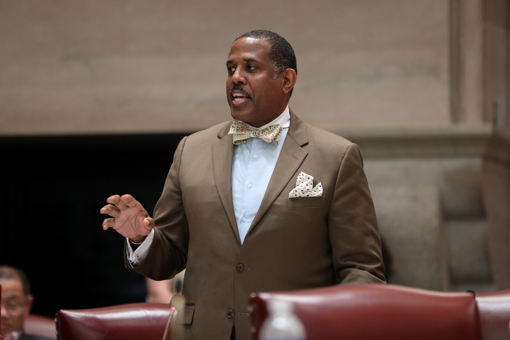 State Sen. Kevin Parker, in a tan suit and white embroidered bow tie, speaks in the Senate chamber in Albany.