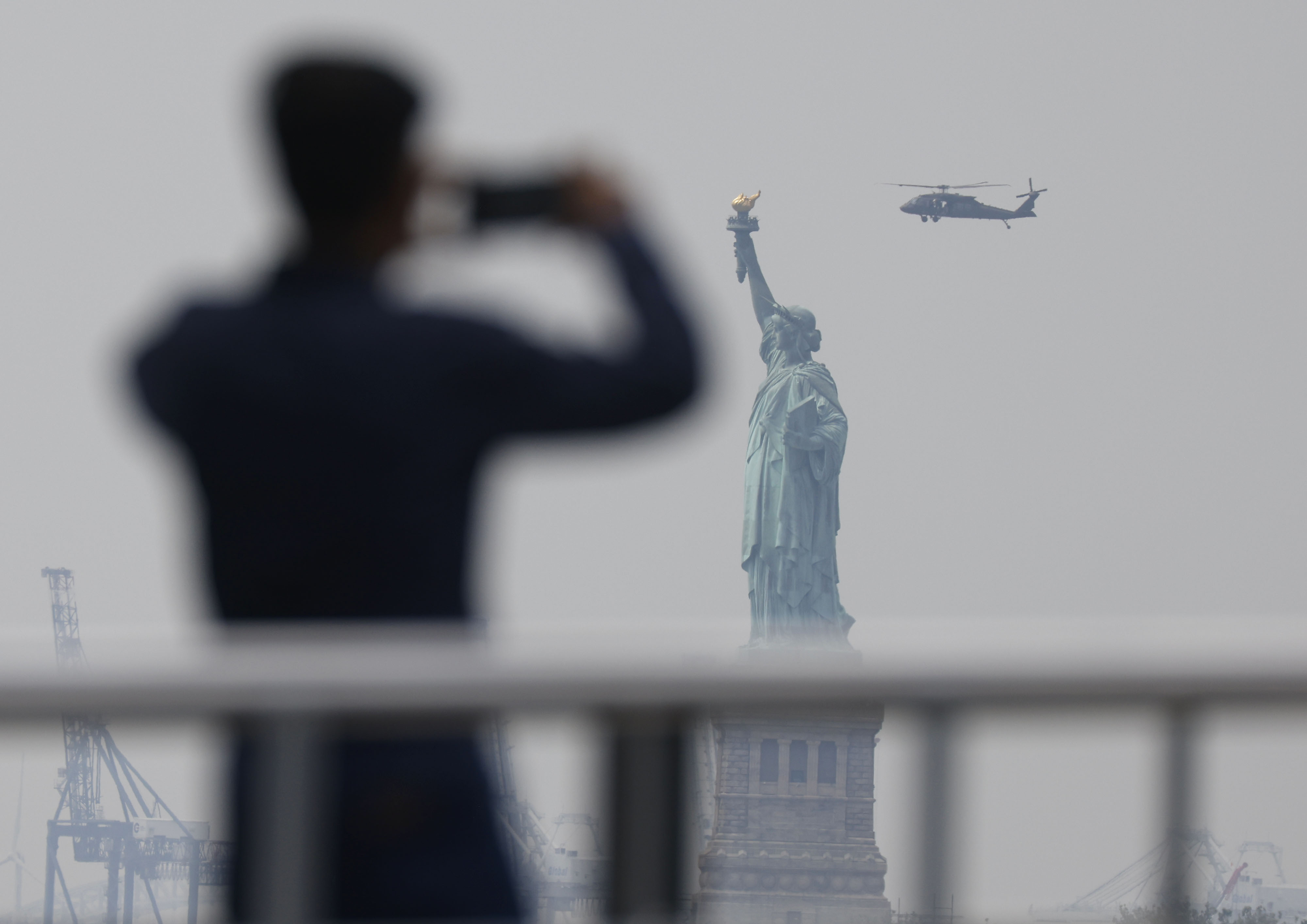 Tourists stand on a ferry before departing to Liberty Island as a haze caused by Canadian wildfire smoke hangs over the Statue of Liberty, June 29, 2023.