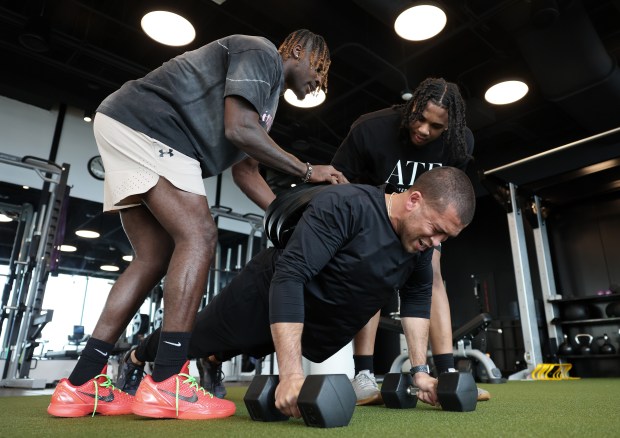 Green Bay Packers wide receiver Jayden Reed, left, and Simeon senior Mikeshun Beeler, a Michigan State signee, place three 45-pound weights on the back of Athletes They Fear founder Kofi Hughes as he does pushups on April 10, 2024, in Chicago. (John J. Kim/Chicago Tribune)