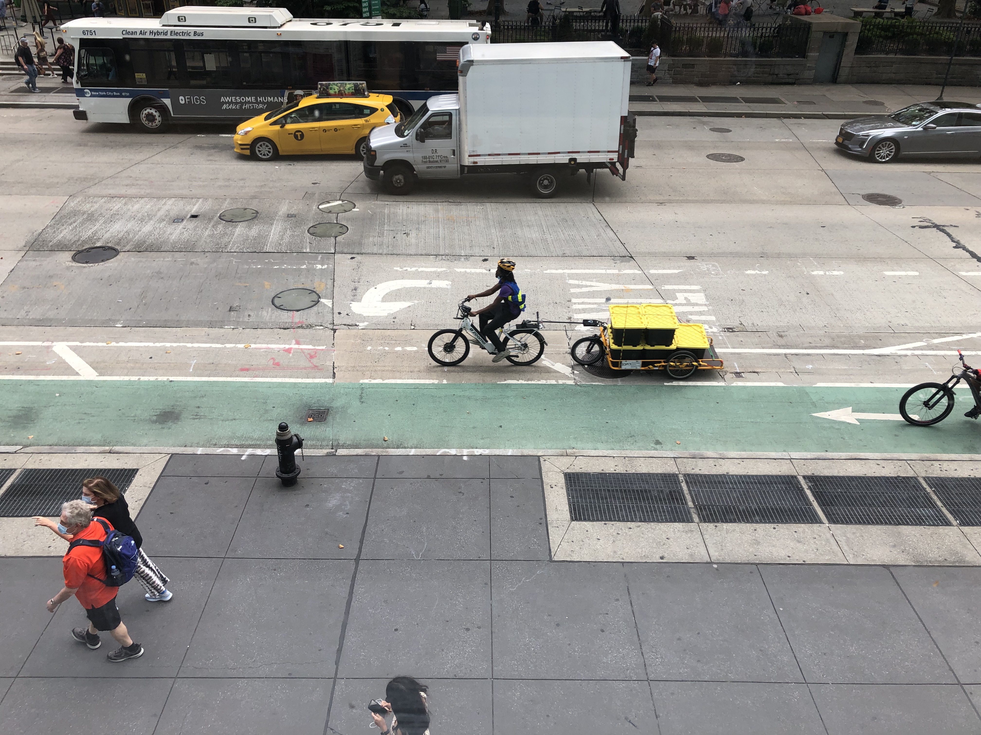 A bike messenger with a trailer in traffic rides along Sixth Avenue near Bryant Park.