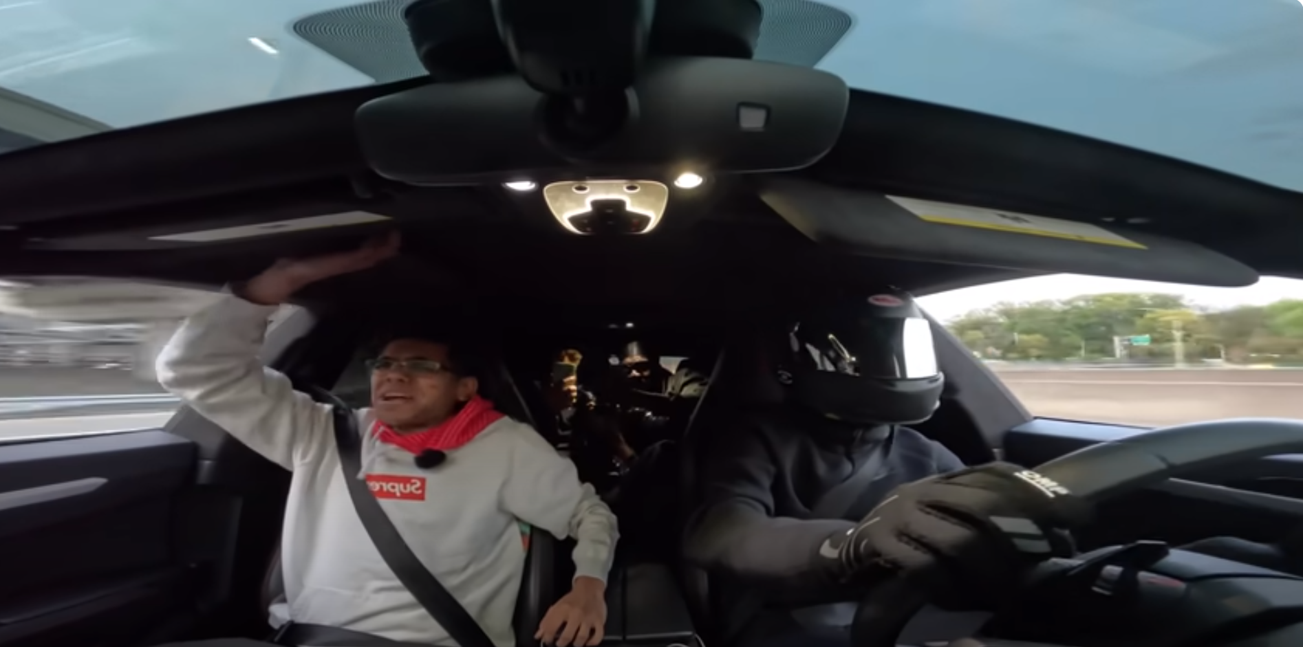 A dashboard cam screengrab of a driver wearing a black helmet and all black, with a passenger screaming in fear.