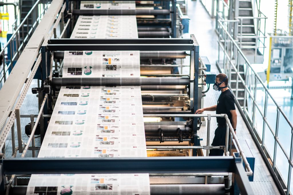 A printing press with several newspapers laid out for print.