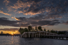 A sailboat sails into the setting sun over the Hudson River and Little Island in Manhattan