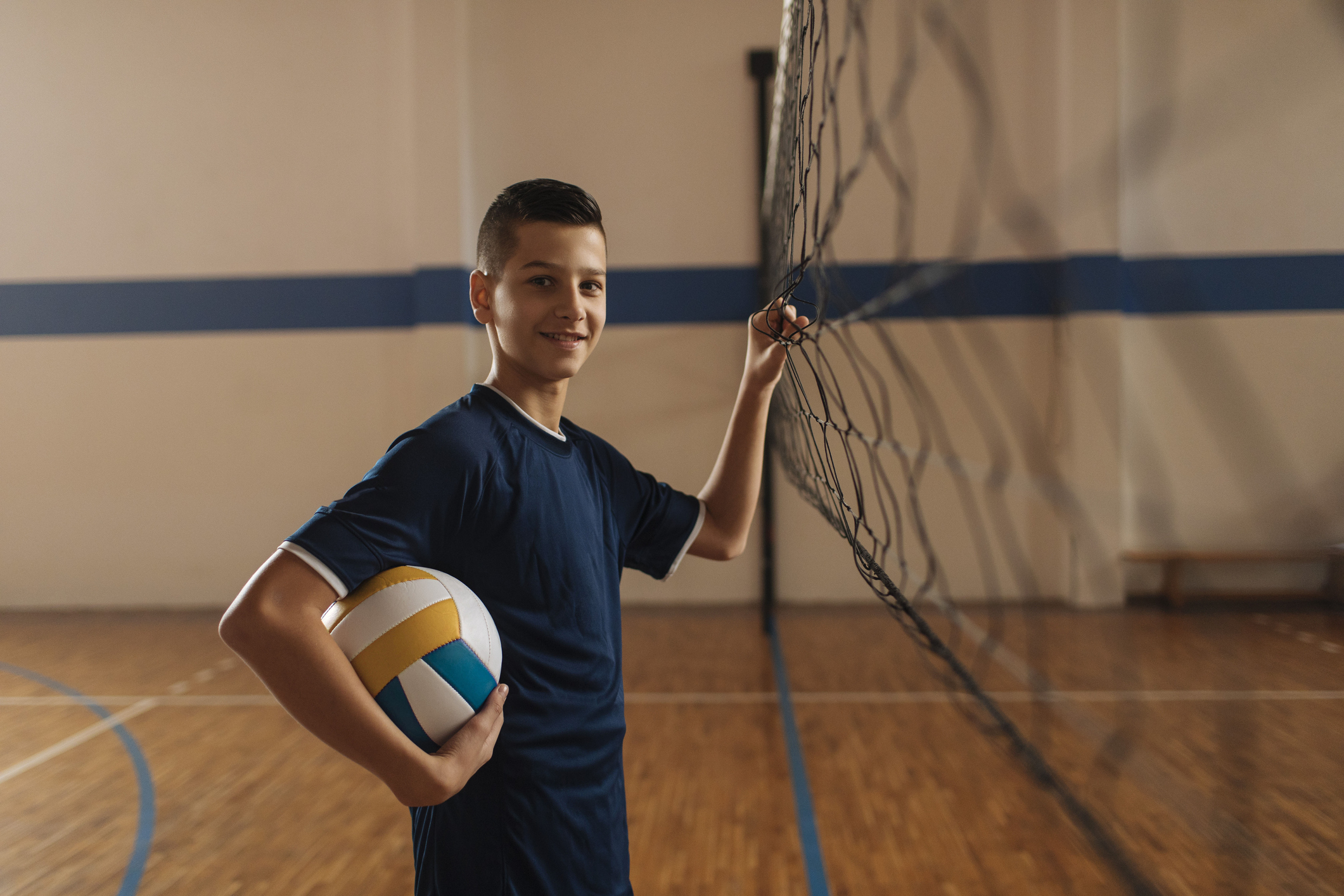 a teen boy holds a volleyball and stands at the net