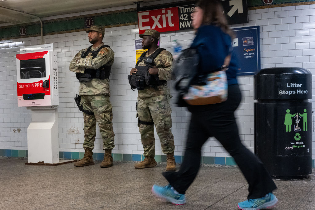 Two National Guard stand along the wall at a subway station.