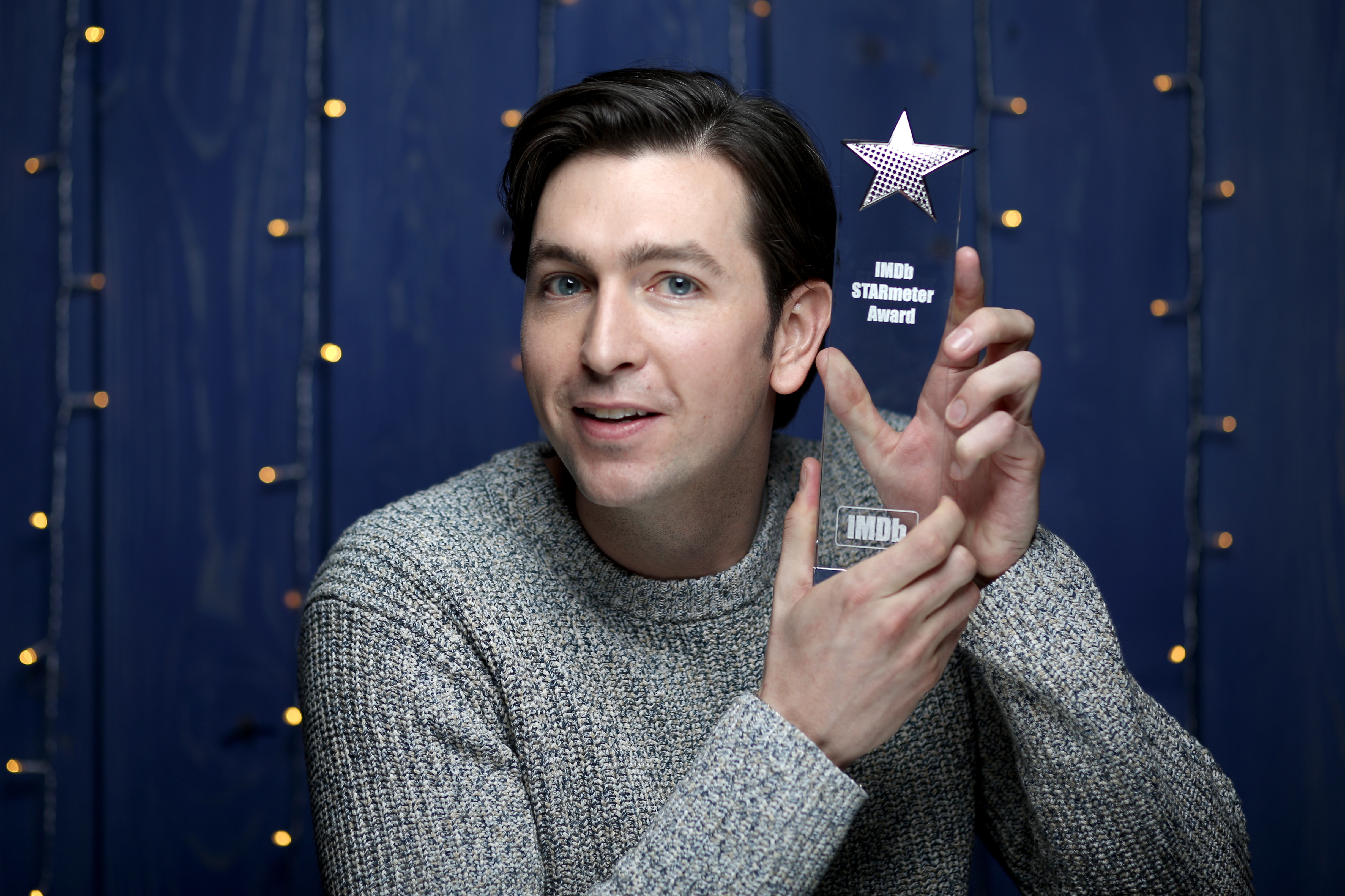 A man in a white sweater holds an award.