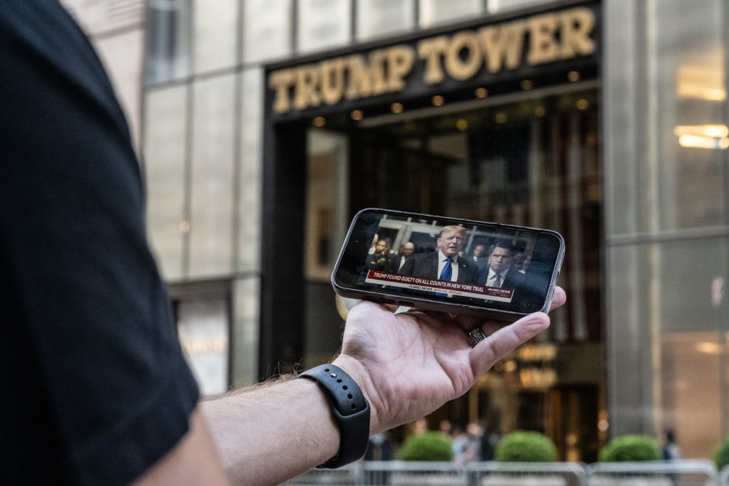 A person looks at their phone as it displays news of the guilty verdict of former U.S. President Donald Trump, with Trump Tower in the background.